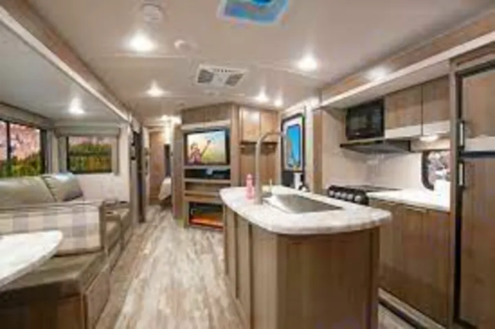 Spacious, modern RV rental interior featuring a kitchen island, living area, and amenities, lit by bright ceiling lights.. Grand Design Imagine 2022