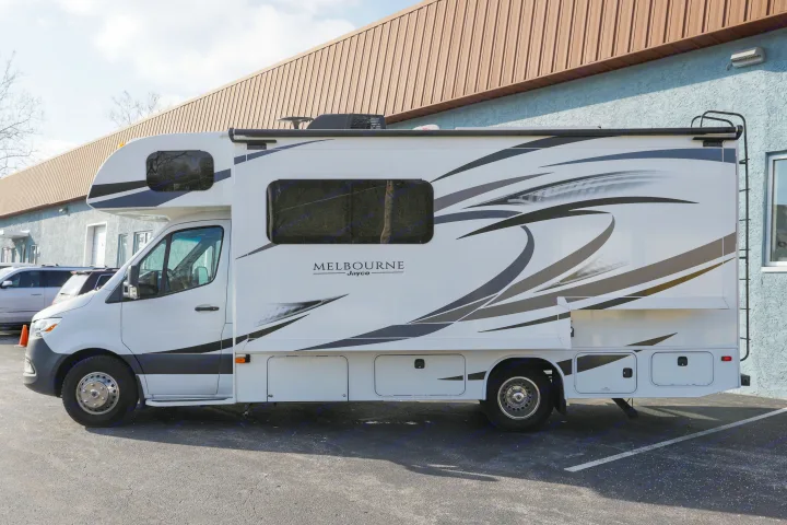 Side view of a white Jayco Melbourne RV rental with black graphics, parked on asphalt near a building.. Jayco Melbourne 2020