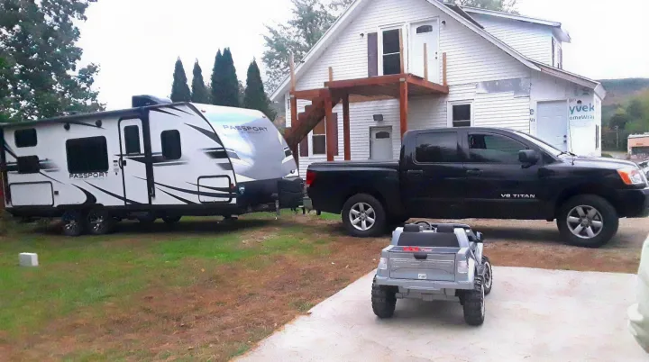 White Passport RV rental, hitched to a black Nissan Titan pickup truck. A small toy truck is in the foreground, with a house in renovation behind.. Keystone RV Passport Express 2019
