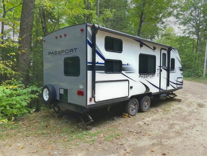 An RV rental: a white & gray Passport travel trailer, parked in a wooded setting, perfect for camping adventures.. Keystone RV Passport Express 2019