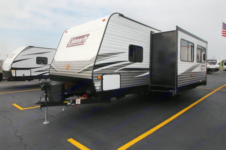 This Coleman RV rental travel trailer with its slide-out extended is parked on a paved lot, ready for adventure.. Dutchmen Coleman 2022
