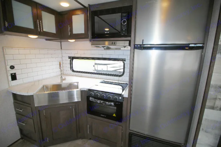 Modern RV rental kitchen with stainless steel fridge, microwave, range, and farmhouse sink, featuring subway tile.. Dutchmen Coleman 2022
