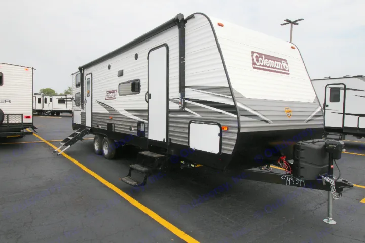White and grey Coleman travel trailer with awning and steps down, perfect for rv rental, parked at a dealer lot.. Dutchmen Coleman 2022
