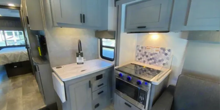 Modern RV rental interior with a bright galley kitchen featuring a stove & sink, leading to a cozy bedroom area in back.. Forest River Solera 2022