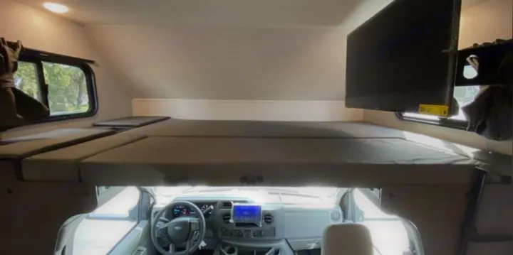 RV rental interior: comfy overhead bunk bed over the front cab, with windows & a mounted TV.. Forest River Solera 2022
