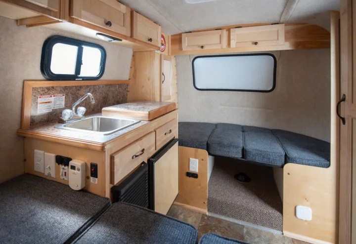 Compact RV rental interior, showcasing a kitchen with sink, refrigerator, light wood cabinets, and a convertible seating/bed.. Scamp Scamp 2021