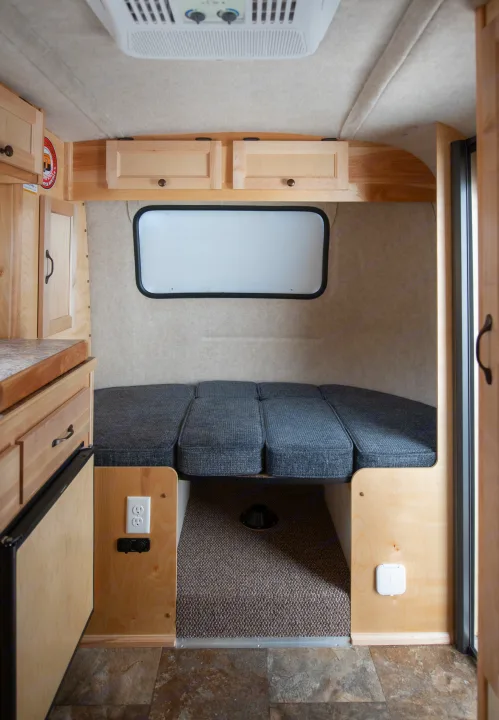 Inside a cozy rv rental camper: grey bed, wood cabinets, AC unit, window, and outlets for comfortable travel.. Scamp Scamp 2021