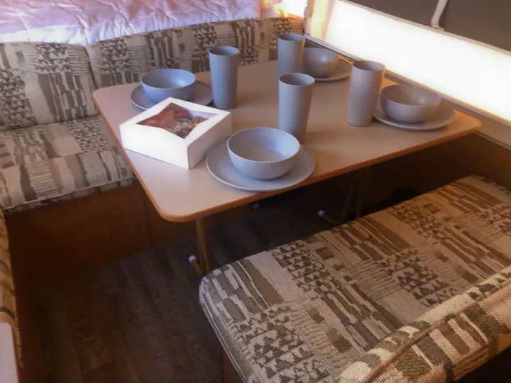 RV rental: Compact dining area with a set table of light gray tableware, patterned cushions, and bed nearby.. Coleman Grand Tour Carmel 2003