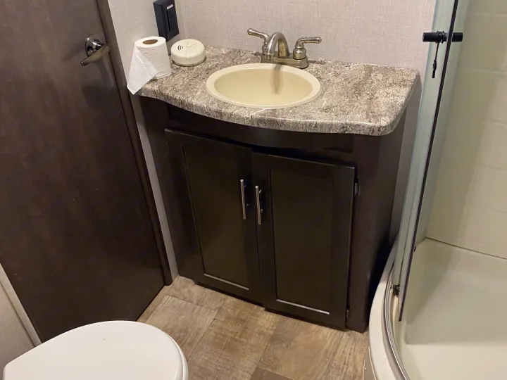 RV rental bathroom with a dark vanity, sink, toilet, and clear shower stall. Toilet paper and a detector are on the counter.. Crossroads Sunset Trail Reserve 2018