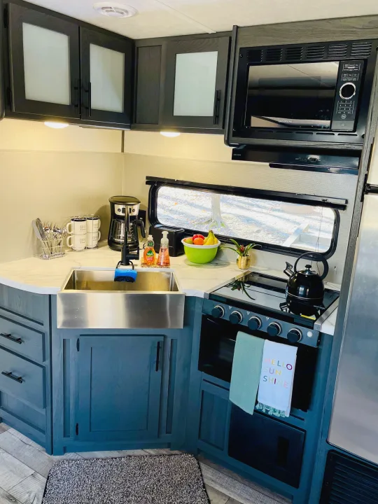Step into this modern RV rental kitchen! Features include dark cabinets, a farmhouse sink, coffee maker, microwave, and stovetop.. Dutchmen Aspen Trail 2022