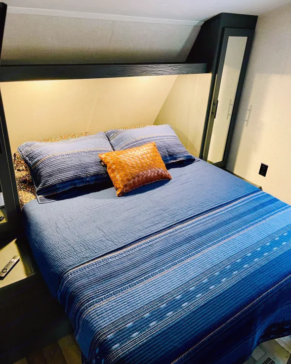 This RV rental's bright bedroom offers a comfy blue quilted bed with accent pillows, built-in lighting, and storage.. Dutchmen Aspen Trail 2022
