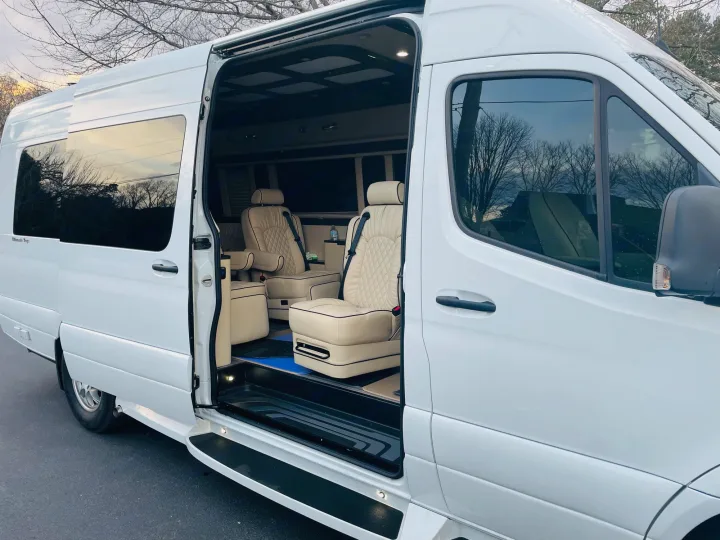 Step inside this white luxury RV rental van with its side door open, revealing plush, diamond-stitched cream seating.. Ultimate Toys Coach- Midwest Automotive Daycruiser D6 2022
