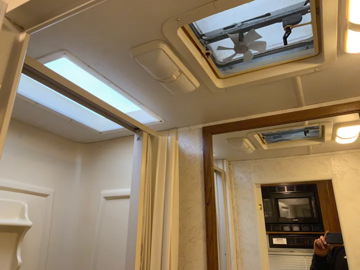 View inside an RV rental: white ceiling with bright skylights and a fan, a mirror reflects a microwave and the photographer.. Thor Motor Coach Chateau 2001