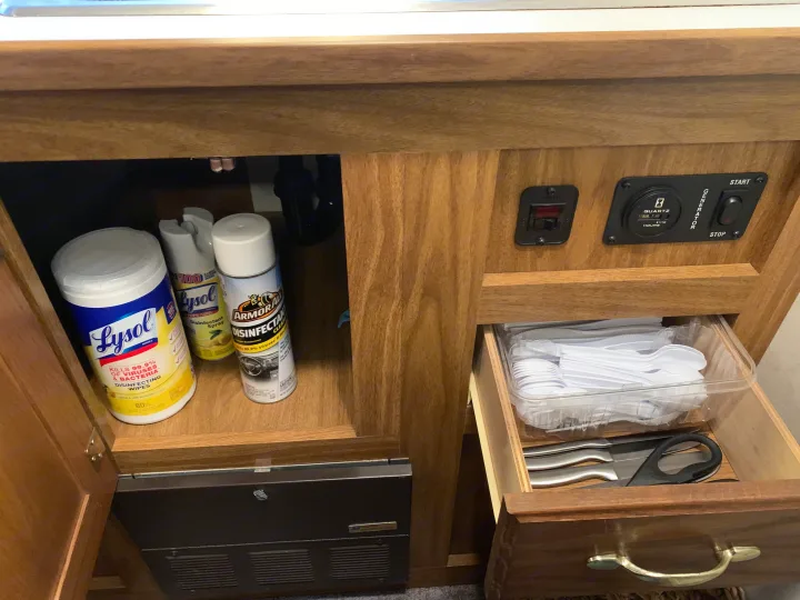 RV rental kitchen storage: Lysol wipes, disinfectant spray, generator controls, and utensils in an open drawer.. Thor Motor Coach Chateau 2001
