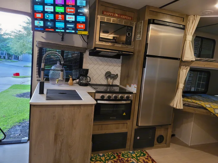 Well-equipped rv rental kitchen & living area with TV, microwave, stove, fridge, and cozy bunk beds.. Forest River Surveyor 2021