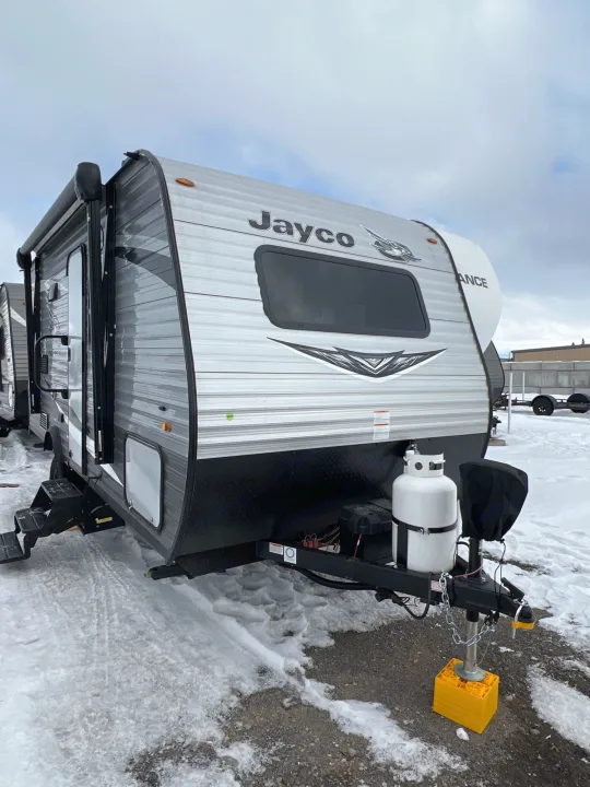 Jayco travel trailer RV rental parked in a snowy lot, equipped with propane tanks and hitch.. Jayco Jay Flight SLX Baja Edition 2021