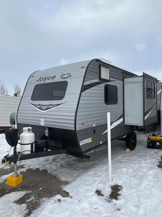 Grey Jayco travel trailer RV rental on a snowy lot, with propane tanks & a generator.. Jayco Jay Flight SLX Baja Edition 2021