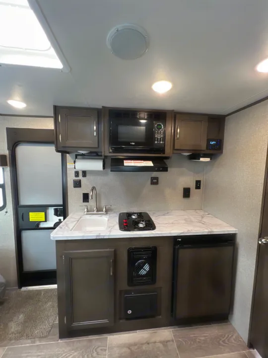 Compact RV rental kitchen featuring a microwave, stove, sink, and under-counter refrigerator.. Jayco Jay Flight SLX Baja Edition 2021