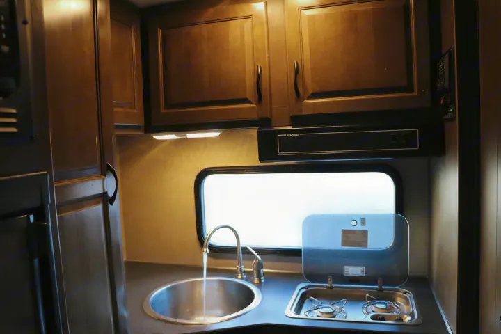 RV rental kitchen: sink with running water, compact two-burner stove, wood cabinetry, window, and overhead lights.. Thor Majestic 2018