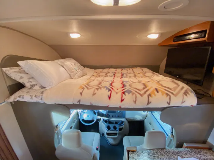 Cozy rv rental cab-over bed area with a TV and entertainment system, overlooking the driver's cabin below.. Jayco Redhawk 2016