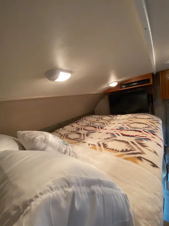 RV rental bedroom interior: bed with patterned blanket, wall lights, and a TV for cozy travels.. Jayco Redhawk 2016