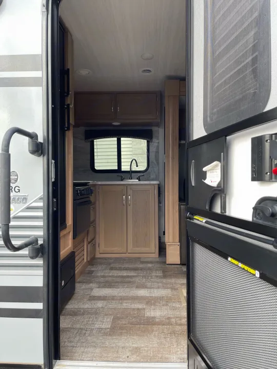 Step into this RV rental! Interior view of a compact kitchen with sink, stove, wood-look floor, seen through the open screen door.. Winnebago Minnie 2020