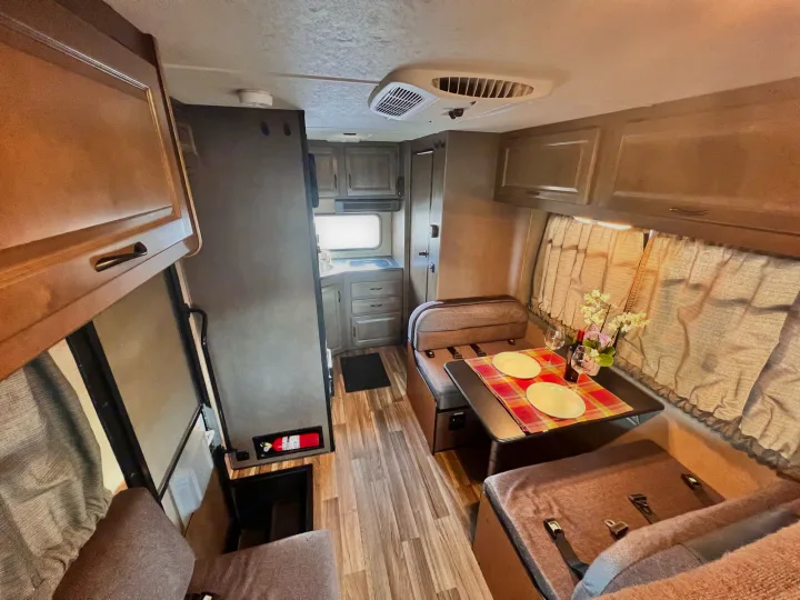 An inviting RV rental interior with a compact kitchen, dinette for meals, comfortable seating, and wood-look flooring.. Thor Majestic 2018