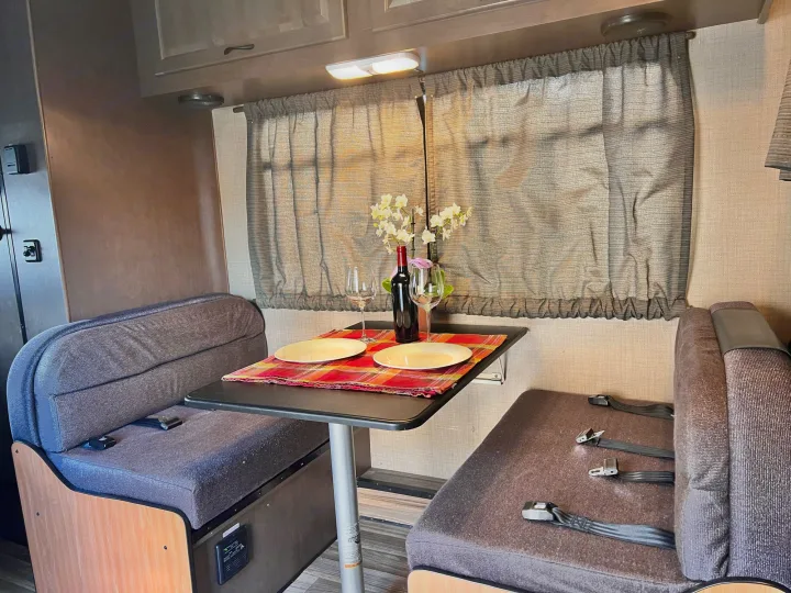 This RV rental shows a charming dinette area with a set table, benches, and window. Ideal for road trip meals.. Thor Majestic 2018