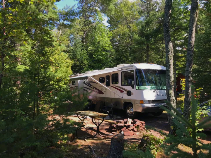 Spacious RV rental parked in a sunny, wooded campsite, complete with a picnic table and fire pit.. Tiffin Motorhomes Allegro Bay 2001