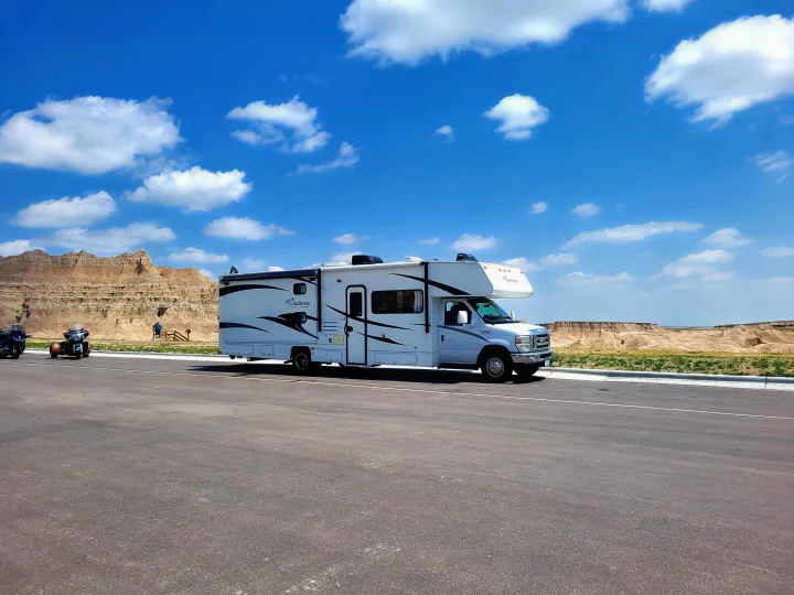 A white Coachmen rv rental is parked on asphalt, offering stunning views of the Badlands rock formations under a bright blue sky.. Other Freelander 2011