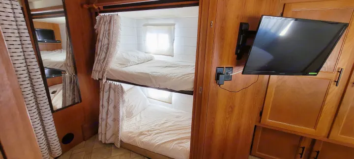 Compact RV rental interior featuring cozy bunk beds with curtains, a wall-mounted TV, and a full-length mirror.. Other Freelander 2011