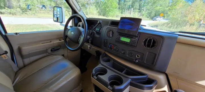 Inside an RV rental, this driver's seat view shows the dashboard, Ford steering wheel, radio, monitor, and cupholders, with a dirt road visible outside.. Other Freelander 2011