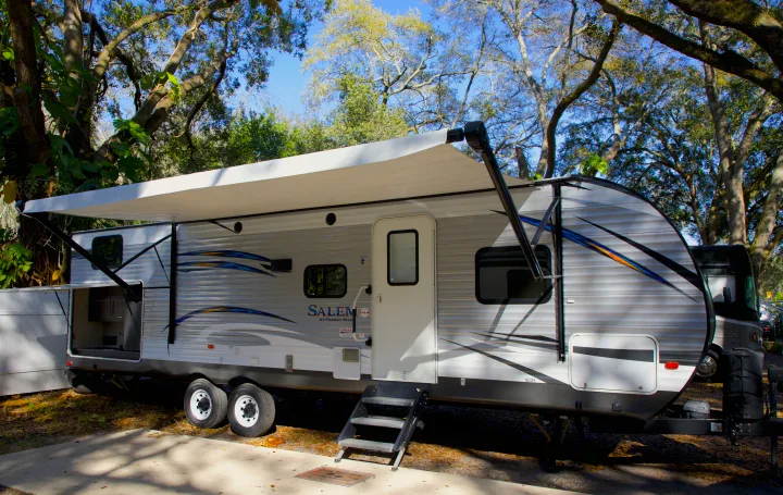 RV rental travel trailer with an extended awning and outdoor kitchen parked at a sunny campsite under large trees.. Forest River Salem 2018