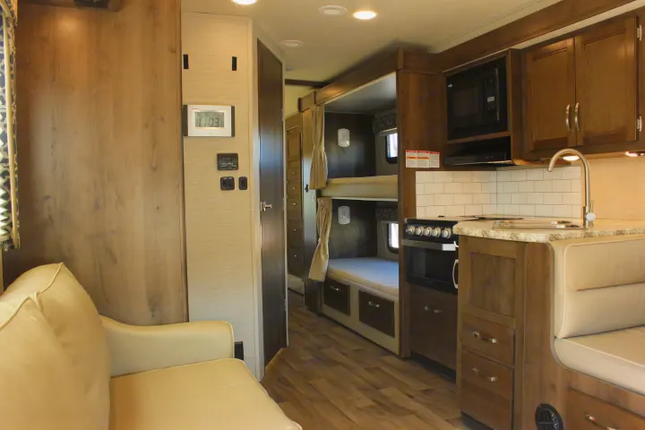 View inside an RV rental, highlighting the kitchen, bunk beds, and lounge area, all in warm wood tones.. Jayco Redhawk 2020