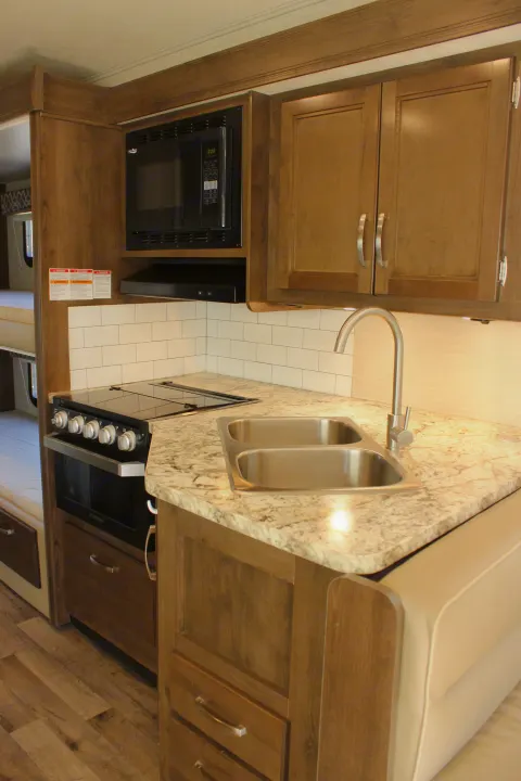 Explore this RV rental's modern kitchen: wood cabinets, granite-look counter, dual sink, microwave, & oven.. Jayco Redhawk 2020