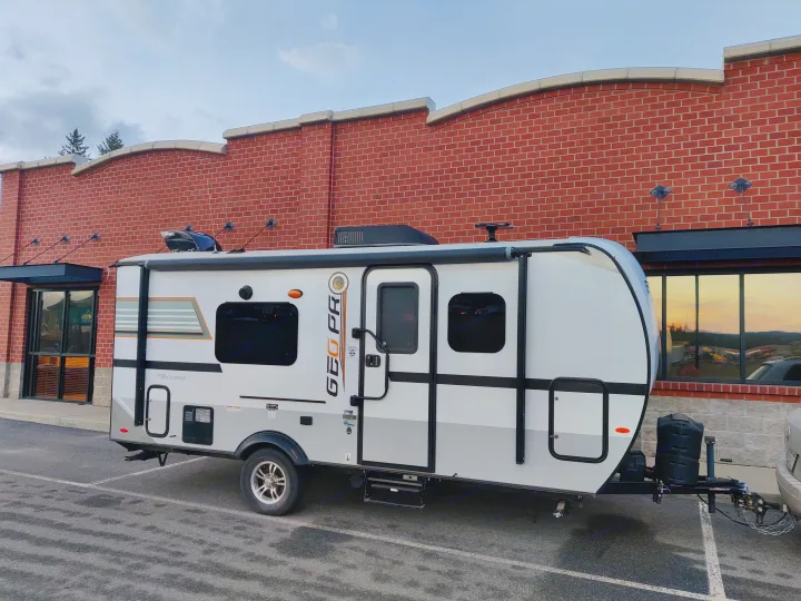 White & gray GEO PRO travel trailer, ready for your RV rental adventure. Parked by a brick building with sunset reflections.. Forest River Geo Pro 2018
