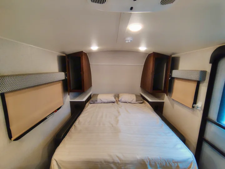 Cozy RV rental bedroom with a comfy bed, overhead cabinets, and window shades, perfect for travel trailer adventures.. Forest River Geo Pro 2018