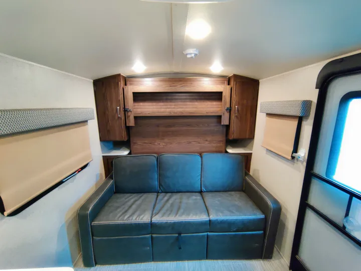 RV rental interior with a dark sofa, wooden overhead cabinets, and window blinds, offering cozy living space for travelers.. Forest River Geo Pro 2018