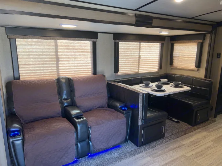 Inside a modern RV rental: plush recliners with cup holders & blue lights, plus a comfy dining booth with a set table.. Grand Design Imagine 2018
