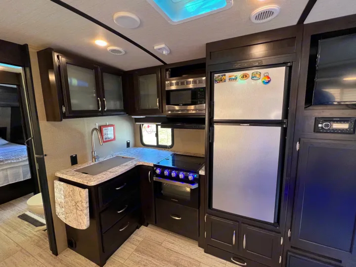 Compact RV rental kitchen with full-size fridge, microwave, stove, sink, and ample cabinet space. Connects to living/bedroom.. Grand Design Imagine 2018