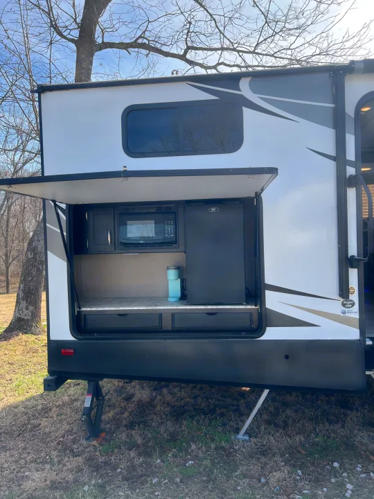 This RV rental features a convenient outdoor kitchen with a microwave, fridge, and counter space, perfect for camping.. Grand Design Imagine 2018