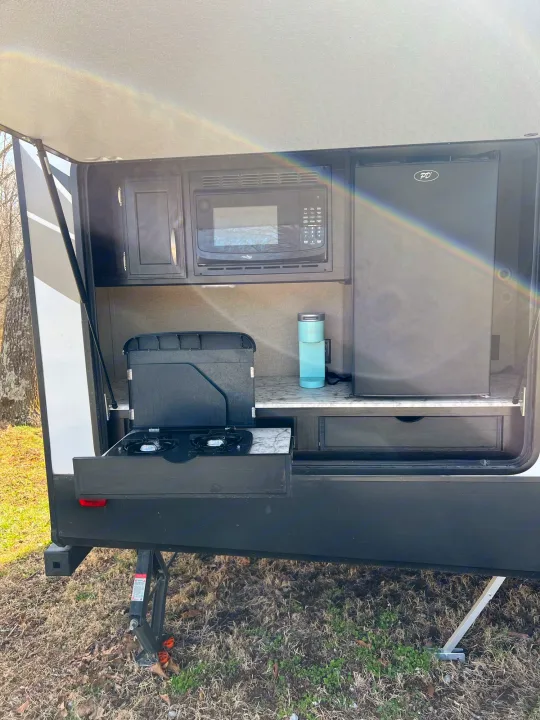 This RV rental boasts a functional outdoor kitchen with microwave, fridge, pull-out stove, and countertop, perfect for camping.. Grand Design Imagine 2018