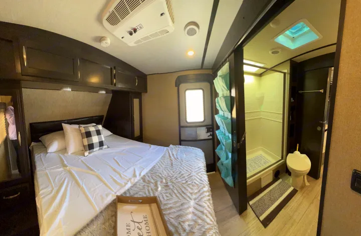 Cozy RV rental interior: bedroom with bed, overhead cabinets, plus a compact bathroom with shower and toilet.. Grand Design Imagine 2018