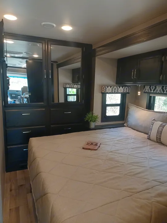 Spacious RV rental bedroom with a cozy bed, dark wood cabinets, and windows, ideal for mobile living and travel.. ENTEGRA VISION A27 2022
