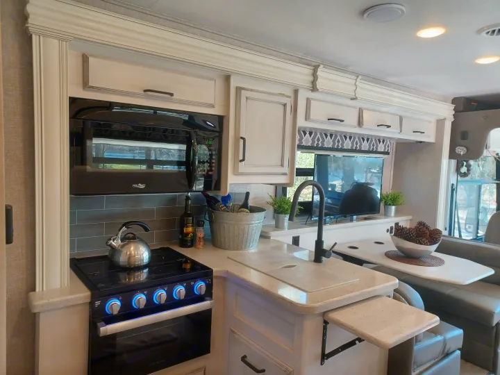 RV rental kitchen with modern amenities: stove, microwave, sink, and dining area. Perfect for a cozy trip.. ENTEGRA VISION A27 2022