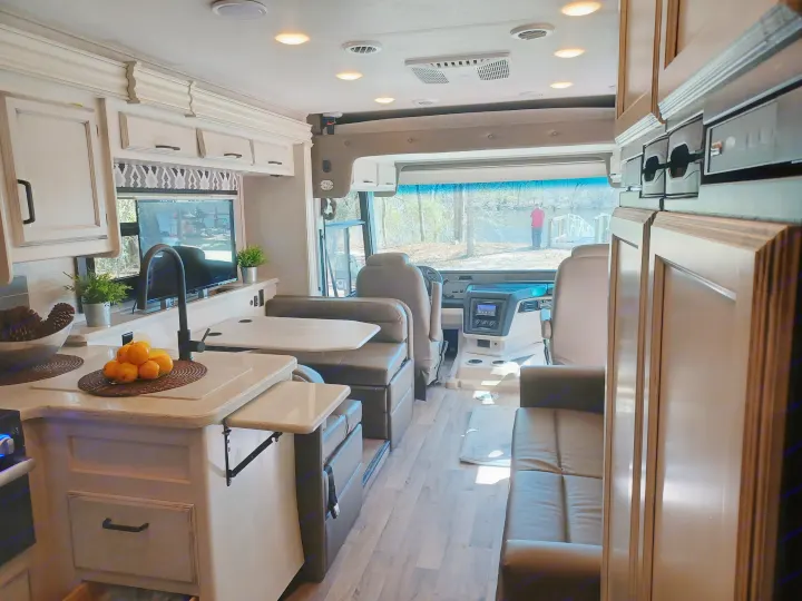 Inside a modern RV rental motorhome: well-lit kitchen, dining, and living areas with a scenic river view from the cockpit.. ENTEGRA VISION A27 2022
