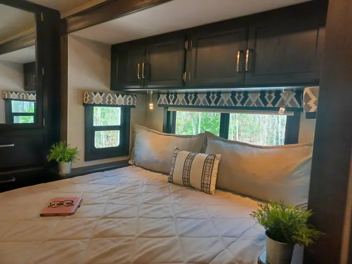 Inside a comfy RV rental: upper sleeping area, windows with nature views, and functional dark wood cabinets.. ENTEGRA VISION A27 2022