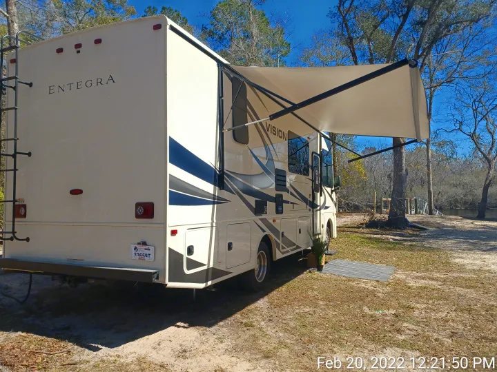 An Entegra Vision rv rental parked at a sunny campsite with its awning extended. Ideal for outdoor travel and camping.. ENTEGRA VISION A27 2022