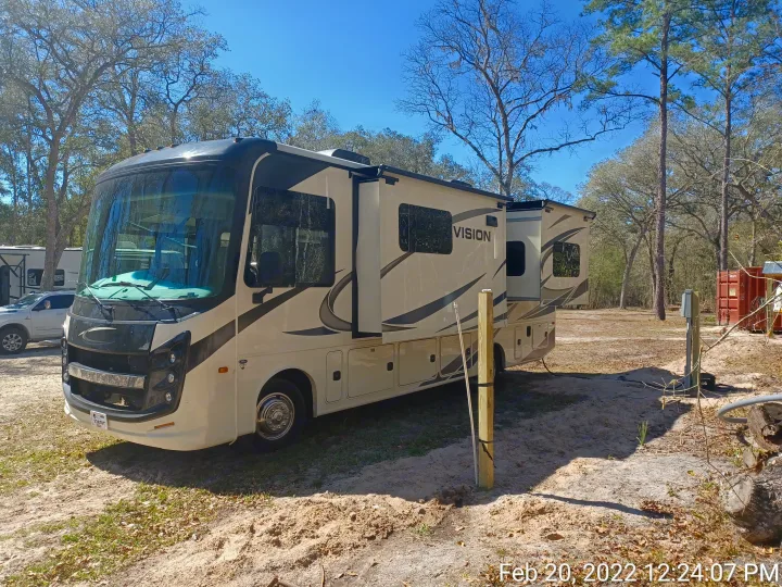 Spacious cream RV rental with extended slide-outs parked on sandy ground at a sunny campsite among trees.. ENTEGRA VISION A27 2022