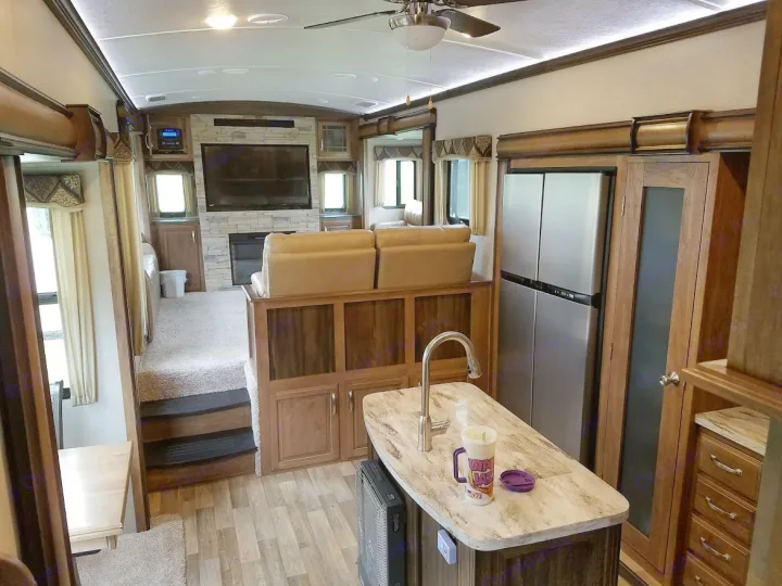 Spacious rv rental interior featuring a modern living area with TV, fireplace, comfy recliners, and full kitchen with island and fridge.. Keystone Montana 2017
